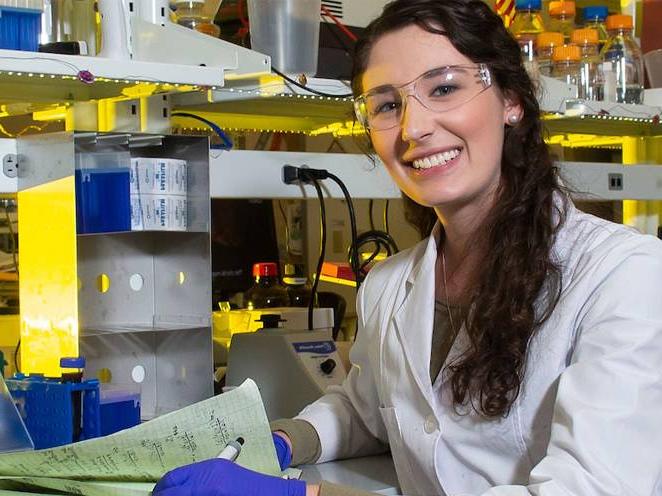 Woman with safety goggles and gloves taking notes and smiling for a picture